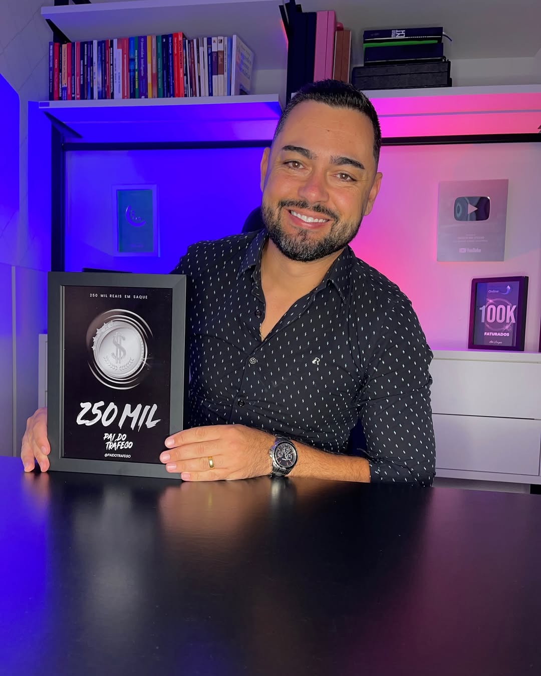 Alex Coelho sorrindo e segurando um quadro comemorativo